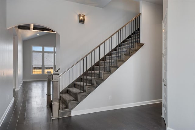 stairs featuring high vaulted ceiling, baseboards, arched walkways, and wood finished floors