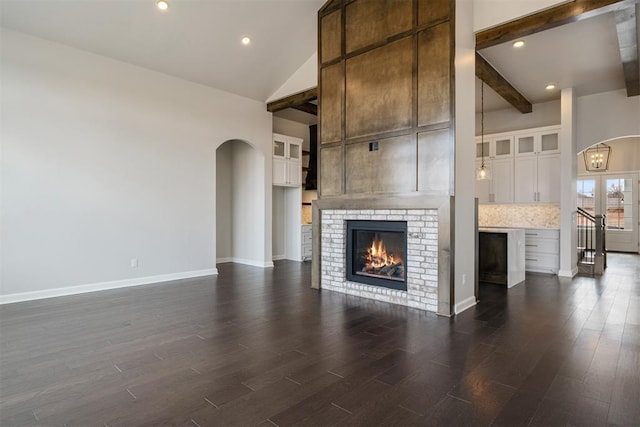 unfurnished living room featuring dark wood-style floors, arched walkways, beam ceiling, a fireplace, and high vaulted ceiling