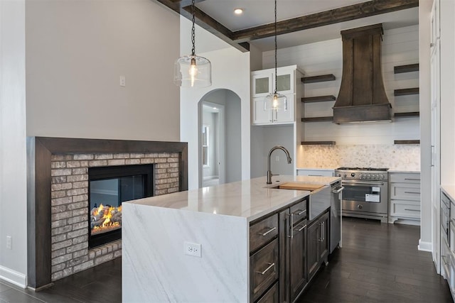 kitchen with a kitchen island with sink, white cabinets, high end range, open shelves, and glass insert cabinets