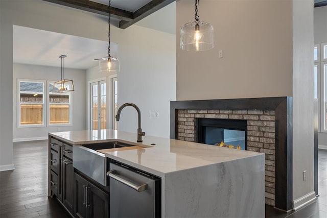 kitchen featuring hanging light fixtures, stainless steel dishwasher, a center island with sink, and light stone counters