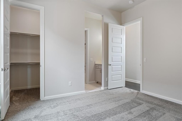 unfurnished bedroom with a walk in closet, a closet, and light colored carpet