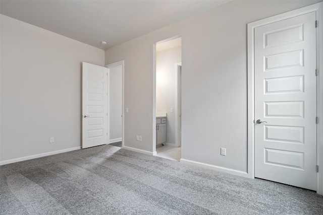 unfurnished bedroom with baseboards, ensuite bathroom, and light colored carpet