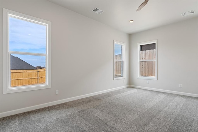 carpeted empty room featuring a healthy amount of sunlight, visible vents, and baseboards