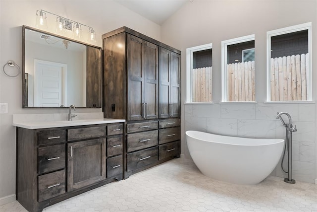 full bath featuring tile walls, a freestanding bath, and vanity