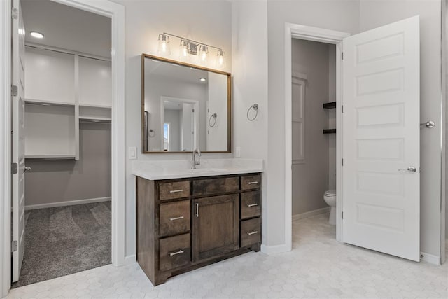 bathroom with a walk in closet, toilet, vanity, and baseboards