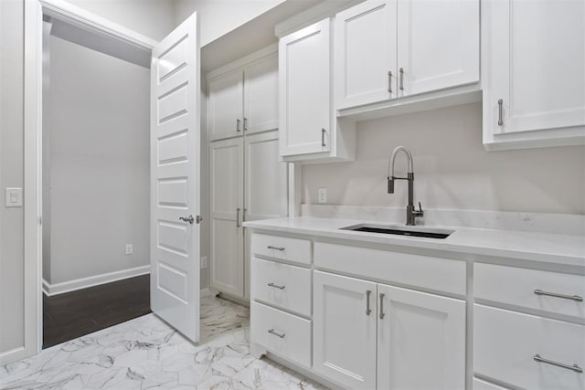 kitchen featuring marble finish floor, light countertops, a sink, and white cabinetry