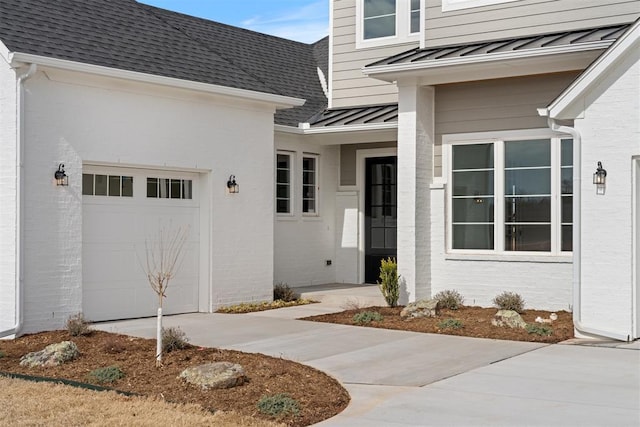 view of exterior entry with a garage, metal roof, roof with shingles, a standing seam roof, and brick siding