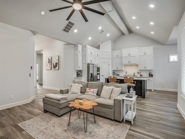 living room with sink, ceiling fan, high vaulted ceiling, beamed ceiling, and light wood-type flooring