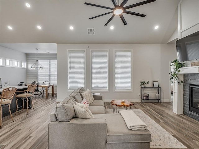 living room featuring vaulted ceiling, ceiling fan, a fireplace, and light hardwood / wood-style floors