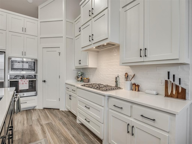 kitchen featuring stainless steel appliances, white cabinetry, light wood-type flooring, and decorative backsplash