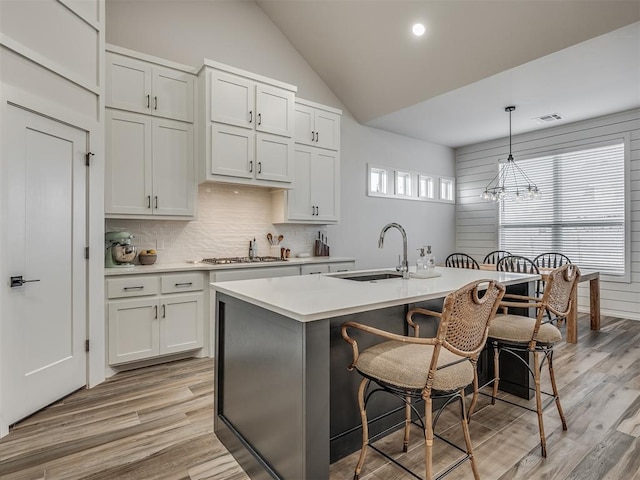 kitchen with pendant lighting, an island with sink, lofted ceiling, a breakfast bar area, and white cabinets