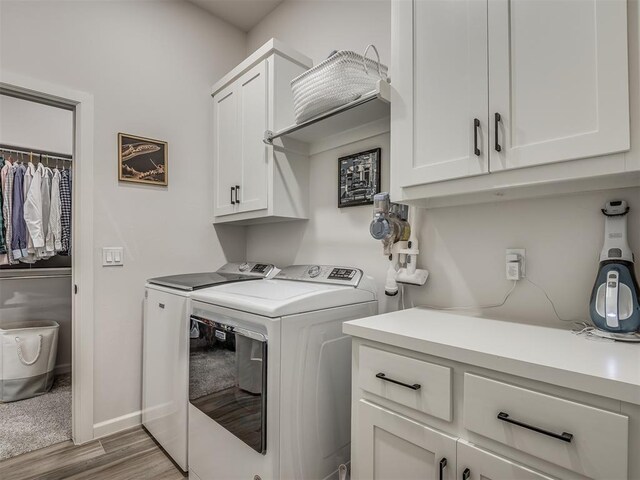 clothes washing area with light hardwood / wood-style flooring, cabinets, and washing machine and clothes dryer