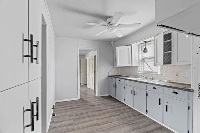 kitchen with sink, white cabinets, backsplash, crown molding, and light wood-type flooring