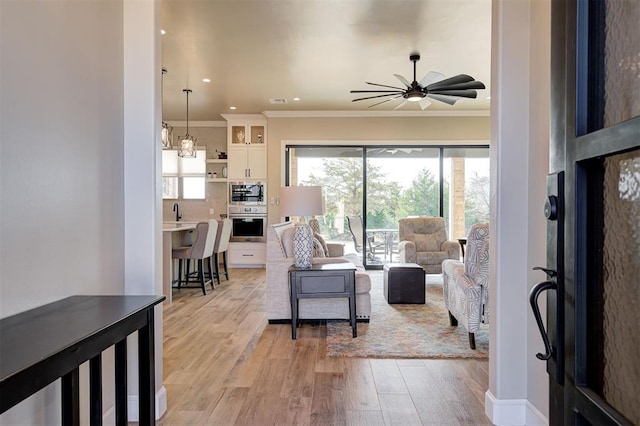 living room featuring ceiling fan, ornamental molding, and light hardwood / wood-style floors