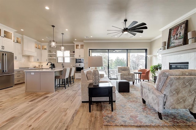 living room with sink, light hardwood / wood-style flooring, a tile fireplace, ceiling fan, and ornamental molding