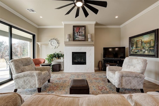 living room with a tiled fireplace, crown molding, ceiling fan, and light wood-type flooring