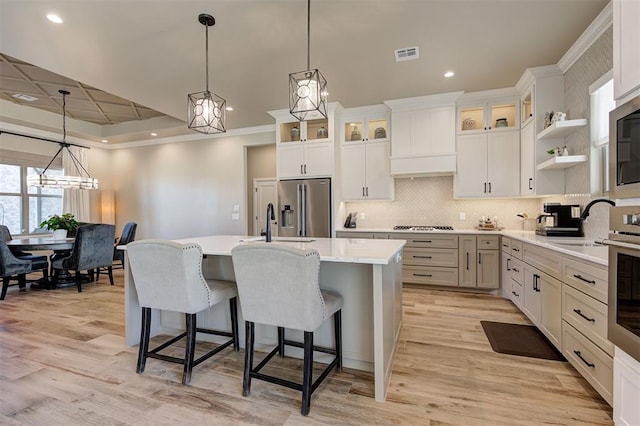 kitchen featuring stainless steel appliances, a kitchen island with sink, white cabinets, and decorative light fixtures