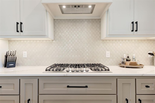 kitchen with tasteful backsplash, extractor fan, light stone countertops, stainless steel gas cooktop, and white cabinets