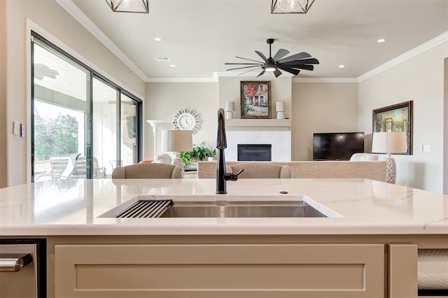 kitchen with crown molding, light stone countertops, sink, and a center island with sink