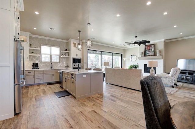 kitchen with pendant lighting, stainless steel appliances, light hardwood / wood-style floors, white cabinets, and a center island with sink