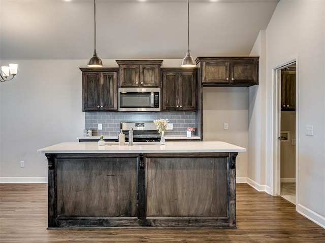 kitchen featuring tasteful backsplash, dark brown cabinets, hanging light fixtures, an island with sink, and stainless steel appliances