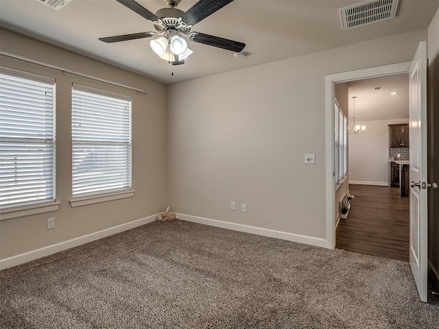 carpeted spare room with ceiling fan with notable chandelier