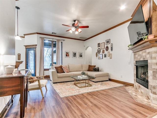 living room featuring a tile fireplace, ornamental molding, ceiling fan, and light wood-type flooring