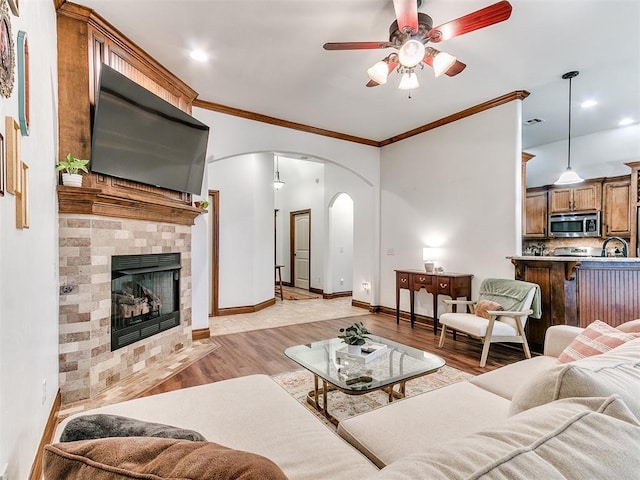 living room with sink, light hardwood / wood-style flooring, ceiling fan, ornamental molding, and a tiled fireplace