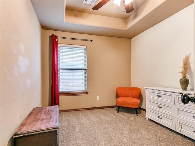 sitting room featuring a raised ceiling, light colored carpet, and ceiling fan