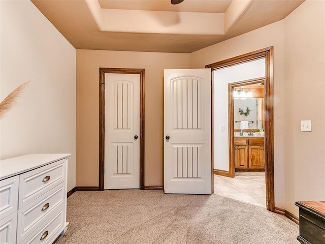 unfurnished bedroom featuring light carpet, sink, ensuite bath, and a raised ceiling