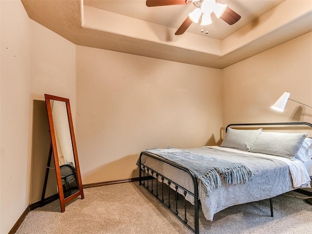 bedroom featuring a raised ceiling, light carpet, and ceiling fan