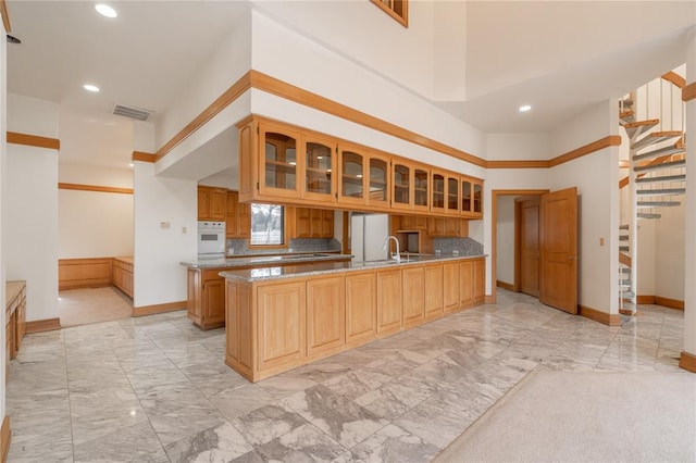 kitchen with marble finish floor, a peninsula, white appliances, and glass insert cabinets