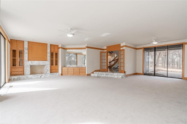 unfurnished living room featuring light carpet, ceiling fan, baseboards, and a premium fireplace