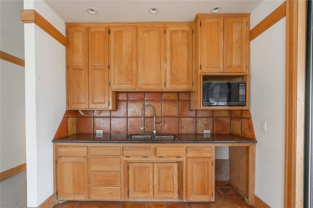 kitchen featuring black microwave, a sink, backsplash, and dark stone countertops