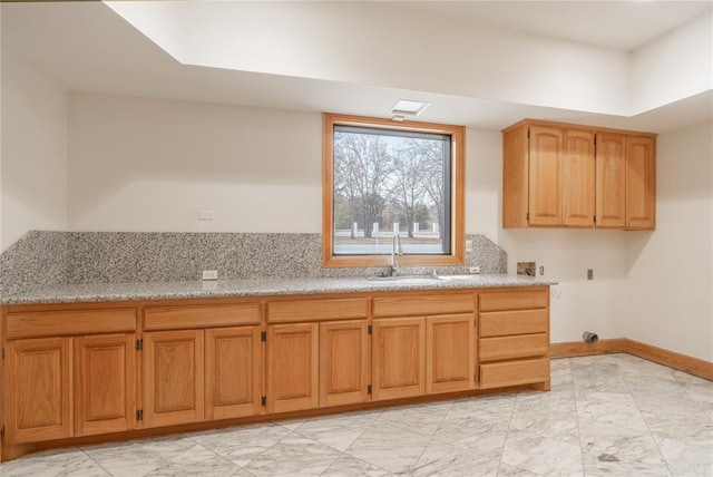 kitchen featuring light stone counters, marble finish floor, a sink, and baseboards