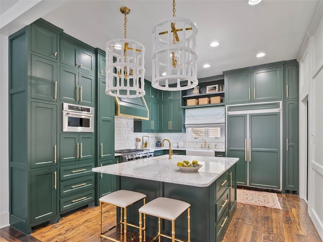 kitchen featuring light stone counters, stainless steel oven, paneled refrigerator, green cabinets, and an island with sink