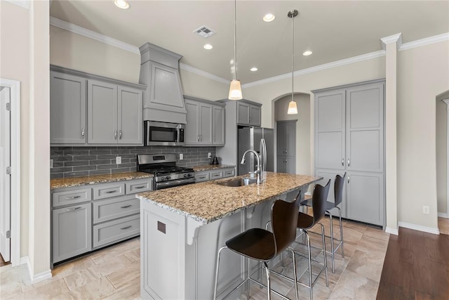 kitchen featuring sink, a kitchen bar, stainless steel appliances, light stone countertops, and a center island with sink