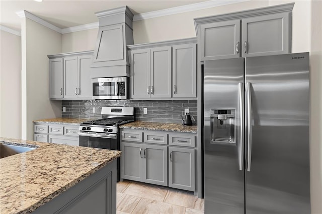 kitchen with gray cabinetry, light stone counters, ornamental molding, stainless steel appliances, and backsplash