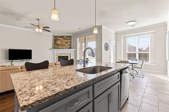 kitchen featuring sink, crown molding, a kitchen island with sink, hanging light fixtures, and light stone counters