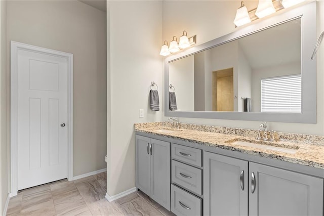 full bath featuring marble finish floor, double vanity, a sink, and baseboards