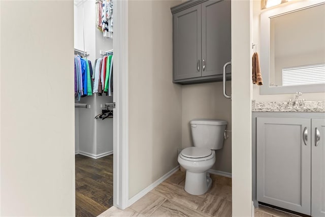 bathroom featuring a spacious closet, vanity, toilet, and baseboards