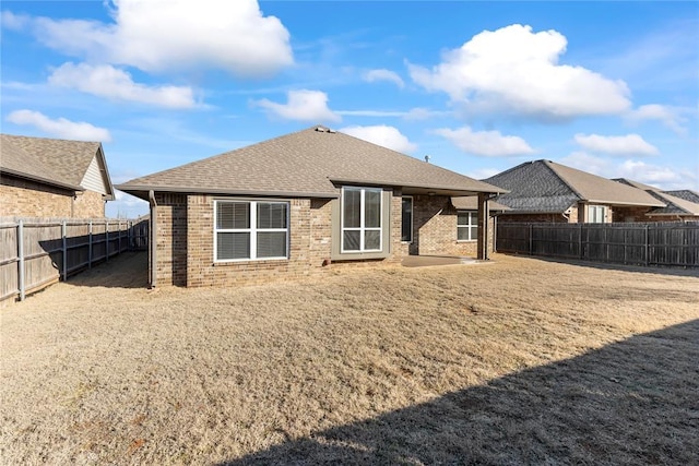 back of property featuring a shingled roof, brick siding, and a fenced backyard