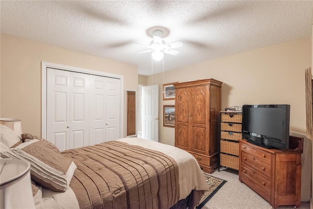 bedroom featuring ceiling fan, light colored carpet, a closet, and a textured ceiling