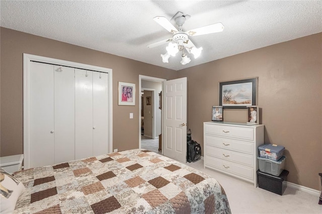 bedroom with light carpet, ceiling fan, a closet, and a textured ceiling