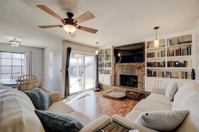 living room with a brick fireplace, wood-type flooring, built in features, and ceiling fan