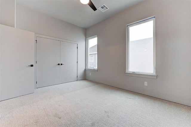 unfurnished bedroom featuring ceiling fan, a closet, light carpet, and multiple windows