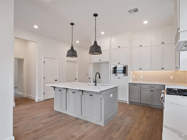 kitchen featuring stainless steel microwave, a sink, decorative backsplash, light wood finished floors, and gas range oven