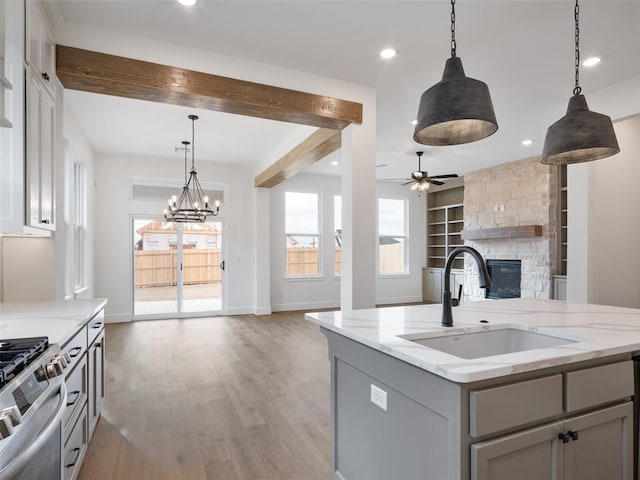 kitchen featuring open floor plan, gray cabinets, a stone fireplace, light wood-type flooring, and a sink