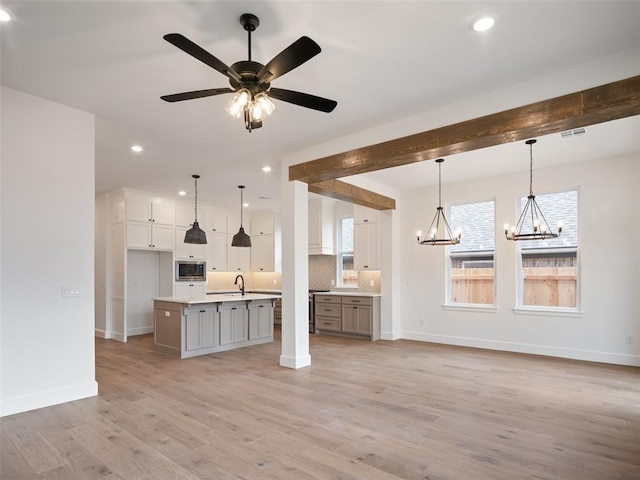 kitchen with tasteful backsplash, a center island with sink, stainless steel microwave, light wood-type flooring, and a sink