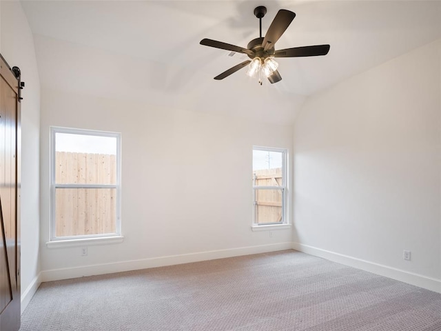 empty room featuring light carpet, a barn door, baseboards, and lofted ceiling